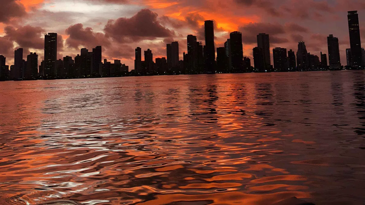 A crowded party boat cruising Cartagena Bay at sunset with the city skyline behind, Colombia